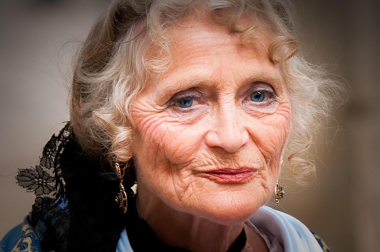 Elegancki portret rudowłosej kobiety o jasnej cerze i niebieskich oczach. Delikatna biżuteria w uszach oraz subtelny makijaż podkreślają naturalny i kobiecy charakter